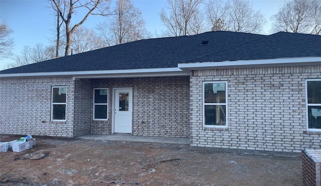 rear view of property with a shingled roof, brick siding, and a patio