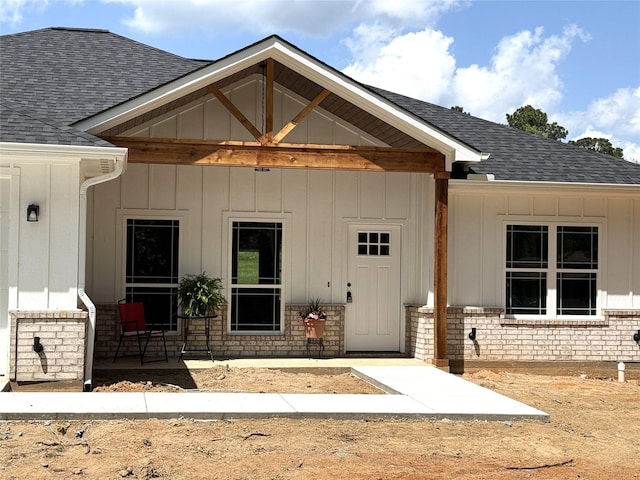 view of exterior entry featuring brick siding, a shingled roof, and board and batten siding