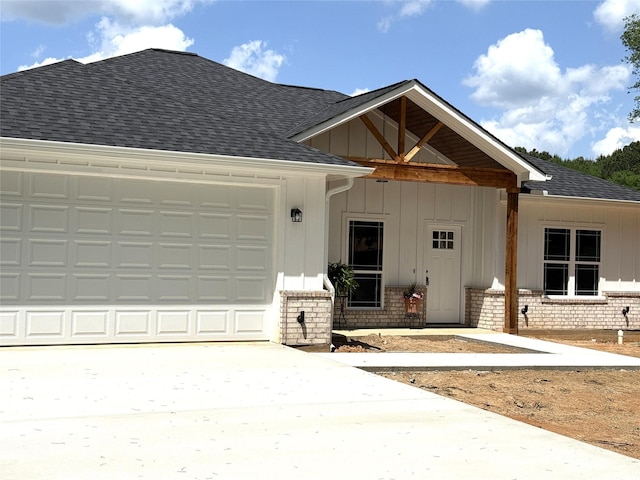 view of front facade featuring driveway, brick siding, a garage, a shingled roof, and board and batten siding
