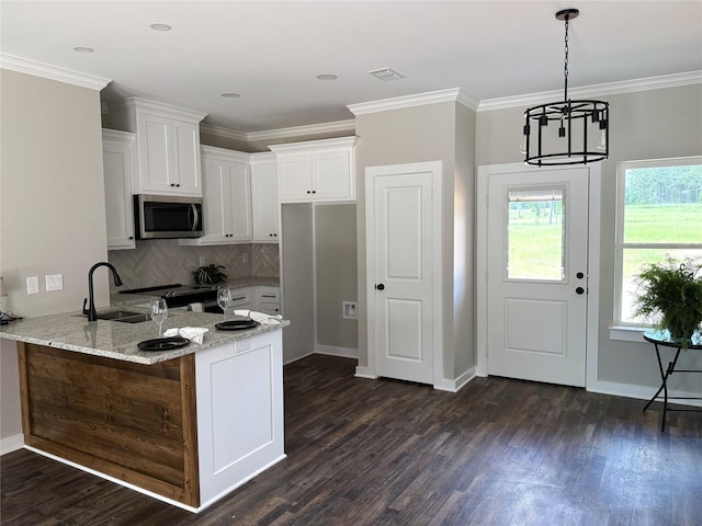 kitchen with light stone counters, a sink, stainless steel microwave, a peninsula, and white cabinetry