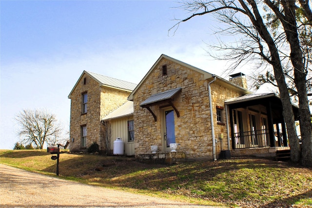 view of front facade featuring metal roof, covered porch, board and batten siding, a chimney, and a front yard