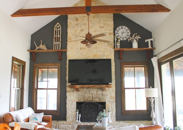 living area featuring vaulted ceiling with beams, ceiling fan, and a stone fireplace