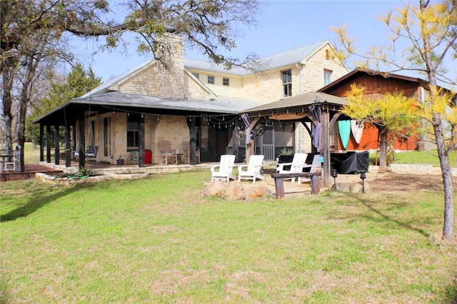 back of property with a lawn, stone siding, a chimney, a gazebo, and a patio area