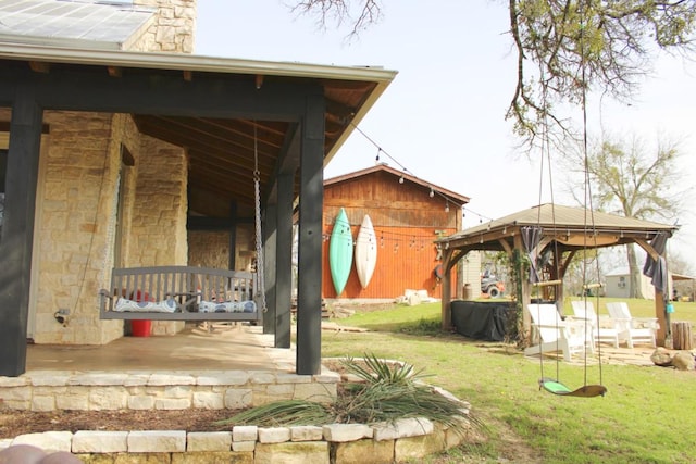 view of side of property with covered porch, a gazebo, stone siding, a lawn, and a chimney