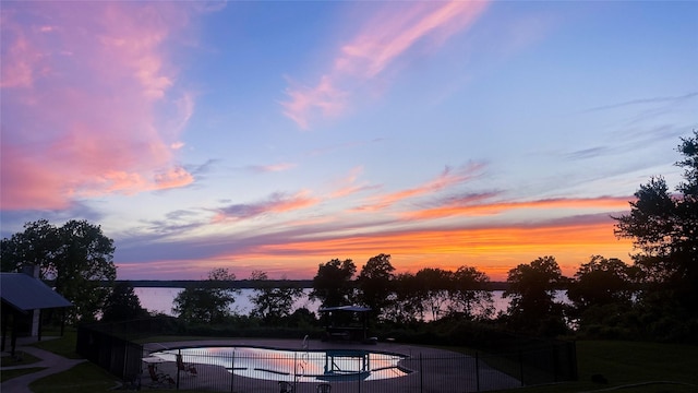 pool at dusk with a water view, fence, and a fenced in pool