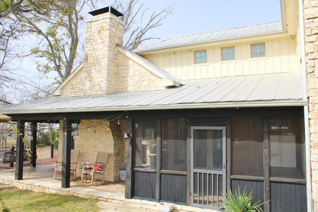 rear view of property featuring a chimney, a sunroom, a patio area, metal roof, and a standing seam roof