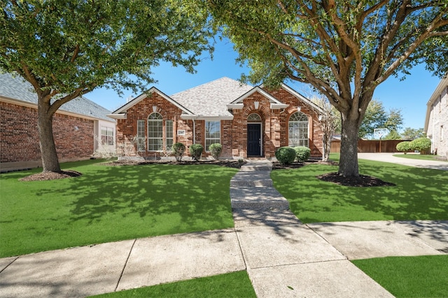 single story home featuring a shingled roof, brick siding, fence, and a front lawn