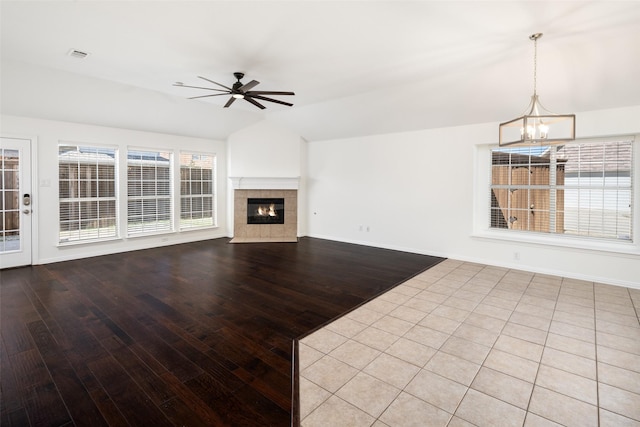 unfurnished living room with lofted ceiling, ceiling fan with notable chandelier, a fireplace, and baseboards