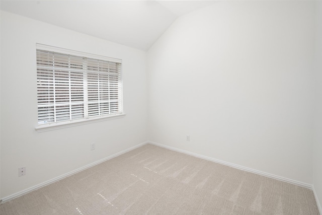 carpeted spare room featuring lofted ceiling and baseboards