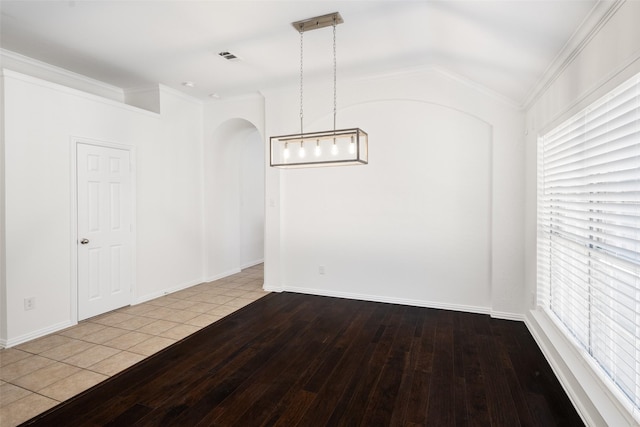 empty room featuring arched walkways, ornamental molding, wood-type flooring, and baseboards