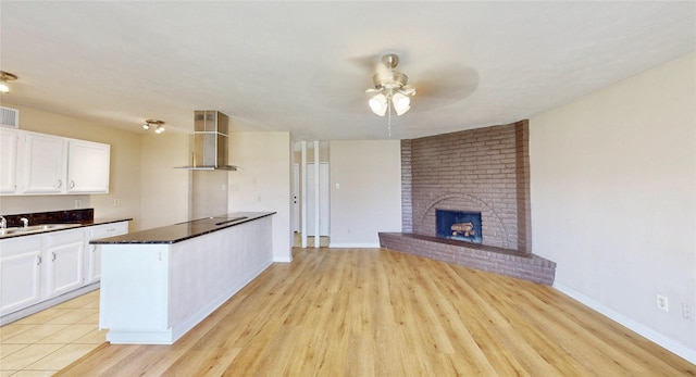 kitchen featuring ceiling fan, wall chimney range hood, a brick fireplace, and white cabinets