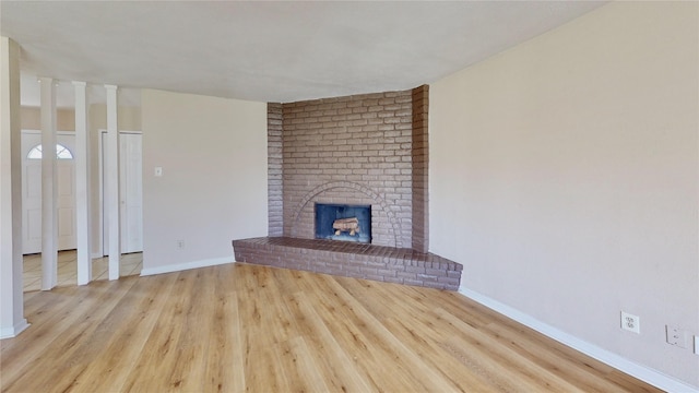 unfurnished living room featuring a brick fireplace, baseboards, and wood finished floors