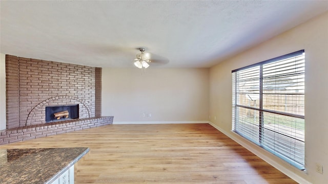 unfurnished living room featuring a textured ceiling, a ceiling fan, baseboards, light wood-type flooring, and a brick fireplace