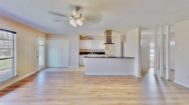 kitchen featuring wall chimney range hood, visible vents, white cabinets, and light wood finished floors