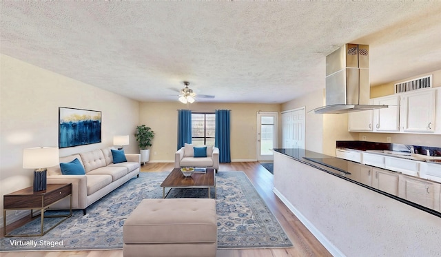 living room featuring ceiling fan, light wood-style flooring, visible vents, and baseboards