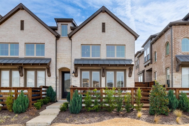 view of front of house featuring stone siding, metal roof, a standing seam roof, fence, and brick siding