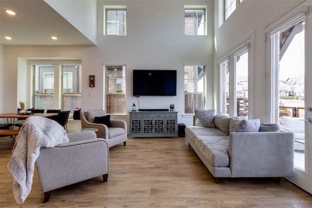 living area with recessed lighting, a healthy amount of sunlight, a high ceiling, and wood finished floors