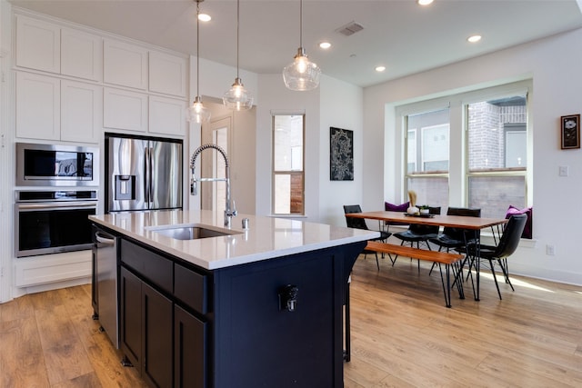 kitchen featuring a sink, visible vents, appliances with stainless steel finishes, light wood finished floors, and decorative light fixtures