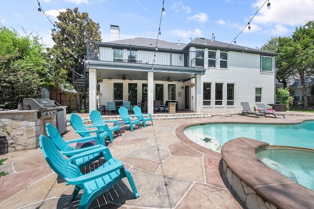 back of property with an outdoor kitchen, a balcony, an in ground hot tub, a ceiling fan, and a patio area