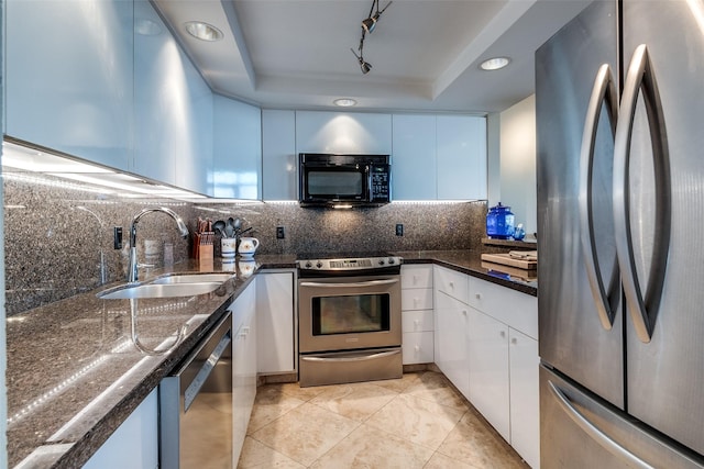 kitchen with a tray ceiling, a sink, stainless steel appliances, white cabinetry, and tasteful backsplash