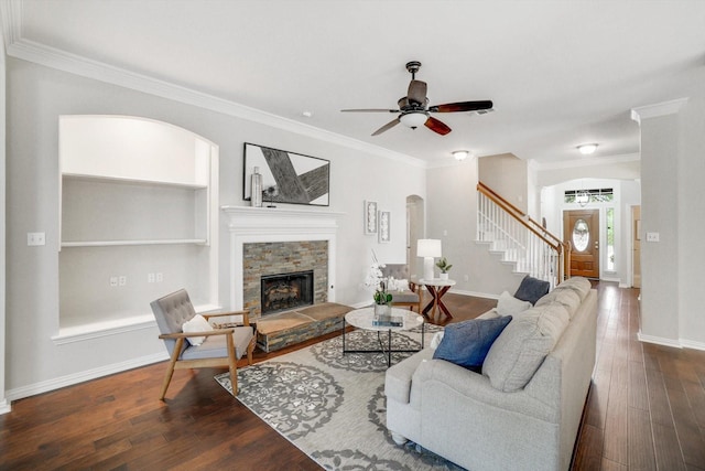 living area featuring dark wood-style floors, ornamental molding, a stone fireplace, baseboards, and stairs