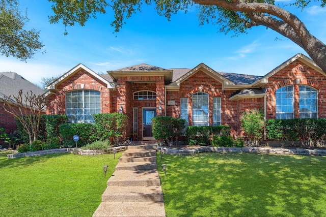 single story home with a shingled roof, a front lawn, and brick siding