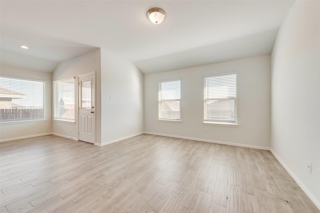 empty room with vaulted ceiling, plenty of natural light, baseboards, and light wood-type flooring