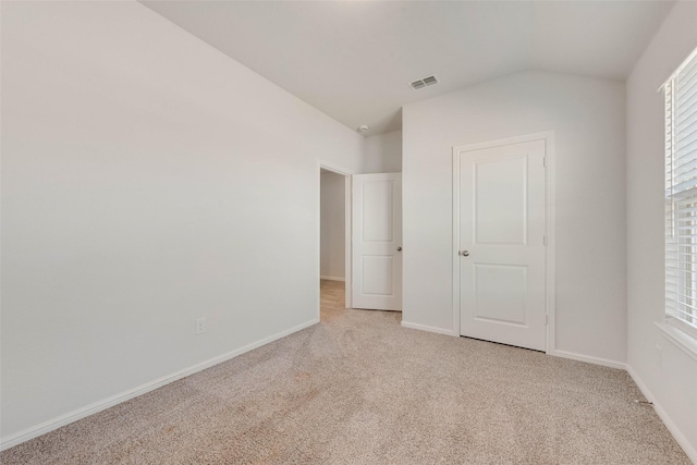 unfurnished bedroom with lofted ceiling, baseboards, visible vents, and light carpet