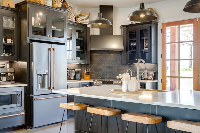 kitchen with backsplash, wall chimney range hood, a breakfast bar area, stainless steel appliances, and a warming drawer