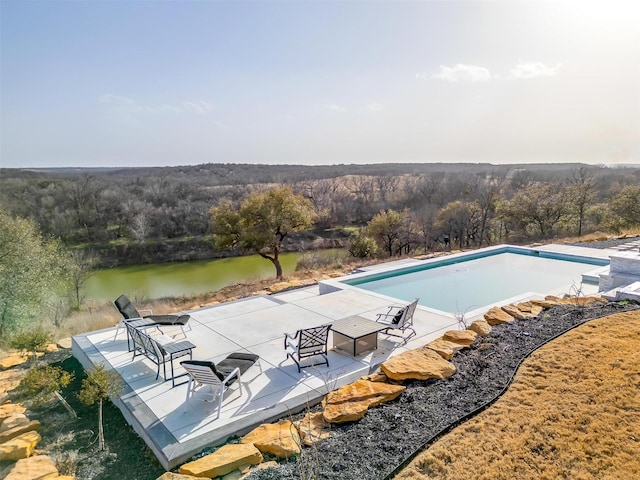 view of pool with a wooded view, an empty pool, a patio, and a water view