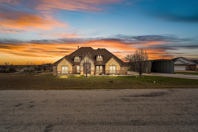 french provincial home featuring driveway, stone siding, fence, a front lawn, and a carport