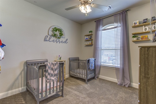 carpeted bedroom featuring a crib, ceiling fan, visible vents, and baseboards