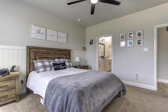 carpeted bedroom featuring ensuite bath, ceiling fan, and wainscoting