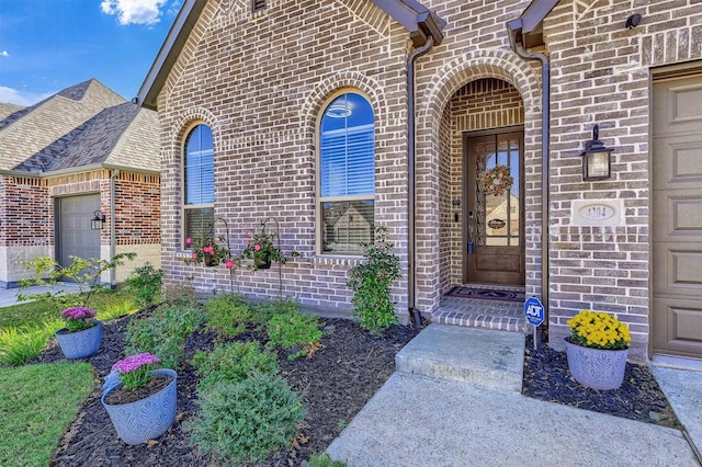 doorway to property with a garage, brick siding, and roof with shingles