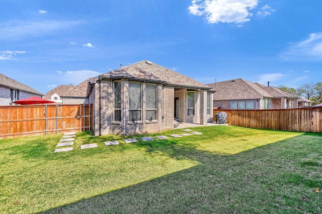 rear view of house with brick siding, a yard, and a fenced backyard