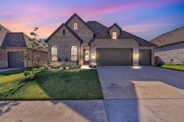 french country inspired facade with a garage, a front yard, concrete driveway, and brick siding