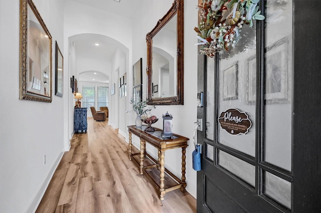 hall featuring arched walkways, light wood-style flooring, baseboards, and recessed lighting