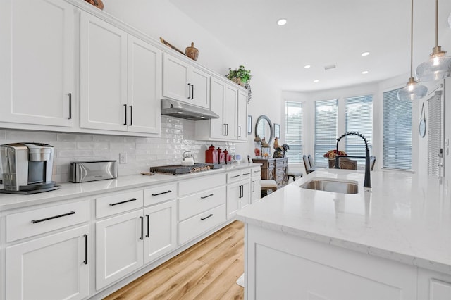 kitchen with tasteful backsplash, under cabinet range hood, stainless steel gas stovetop, white cabinetry, and a sink