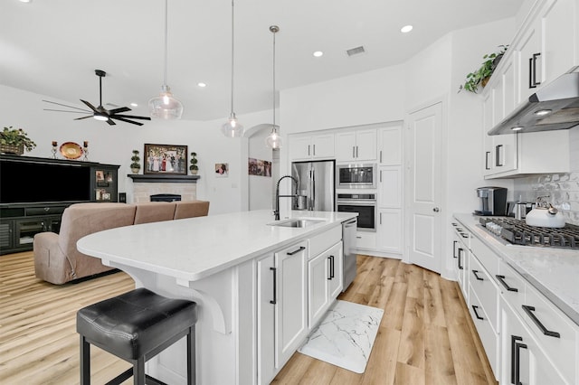 kitchen featuring light wood finished floors, tasteful backsplash, arched walkways, appliances with stainless steel finishes, and a sink