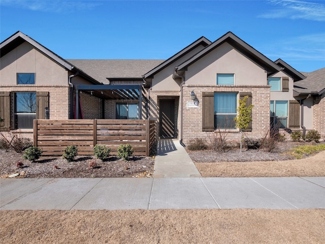 view of front facade with stucco siding, fence, and brick siding