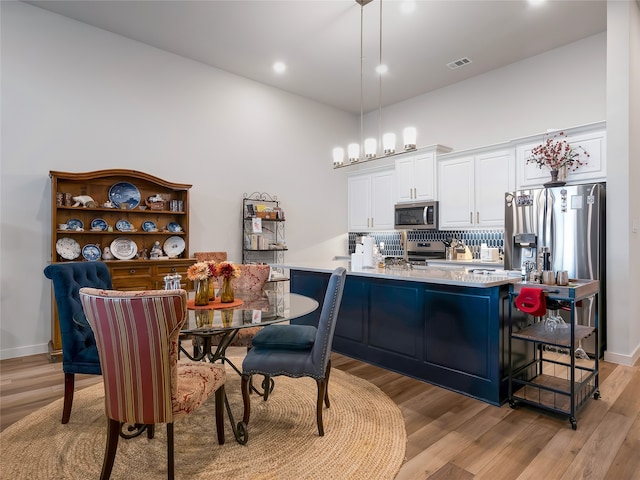 kitchen featuring tasteful backsplash, light countertops, appliances with stainless steel finishes, white cabinets, and light wood-type flooring