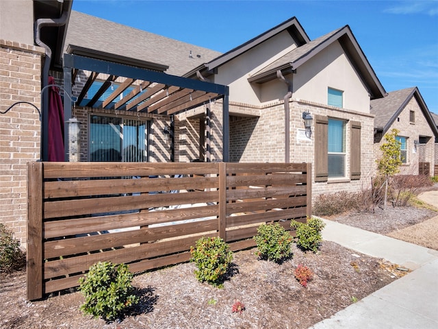 view of front of property featuring brick siding, a pergola, fence, and stucco siding