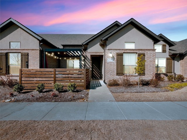 view of front of home with stucco siding, a shingled roof, fence, and brick siding