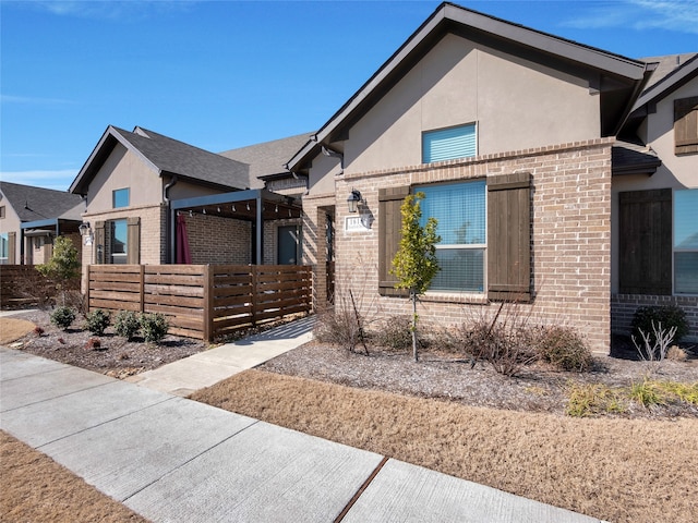 view of front of property with brick siding, fence, and stucco siding