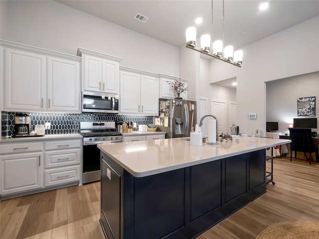 kitchen with visible vents, appliances with stainless steel finishes, light wood-type flooring, tasteful backsplash, and a center island with sink