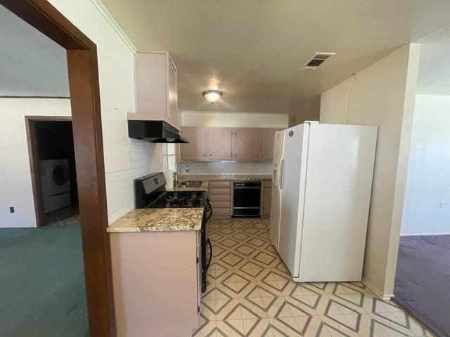 kitchen featuring gas stove, visible vents, washer / dryer, freestanding refrigerator, and under cabinet range hood