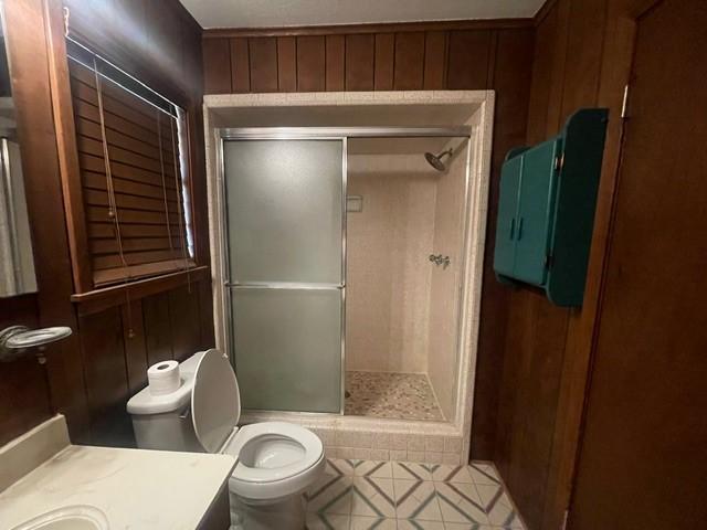 full bathroom featuring tile patterned flooring, wooden walls, toilet, a stall shower, and vanity