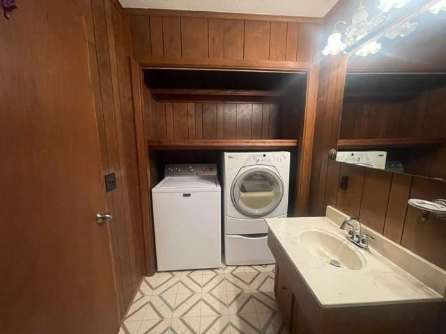 washroom with a sink, separate washer and dryer, wood walls, and laundry area