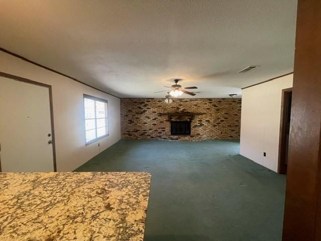 unfurnished living room with visible vents, a textured ceiling, brick wall, a fireplace, and ceiling fan