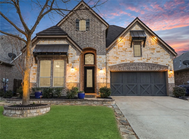 french provincial home with brick siding, concrete driveway, stone siding, an attached garage, and a front yard